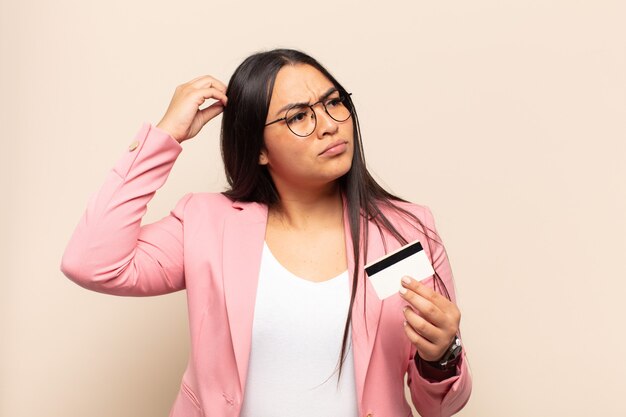 Young latin woman feeling puzzled and confused, scratching head and looking to the side