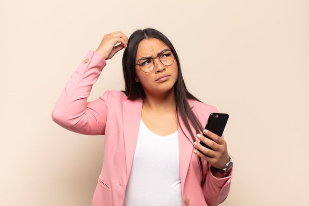 Young latin woman feeling puzzled and confused, scratching head and looking to the side