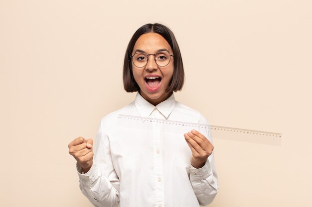 Young latin woman feeling shocked, excited and happy, laughing and celebrating success, saying wow!