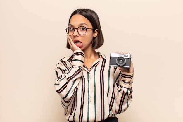 Young latin woman feeling shocked and scared, looking terrified with open mouth and hands on cheeks