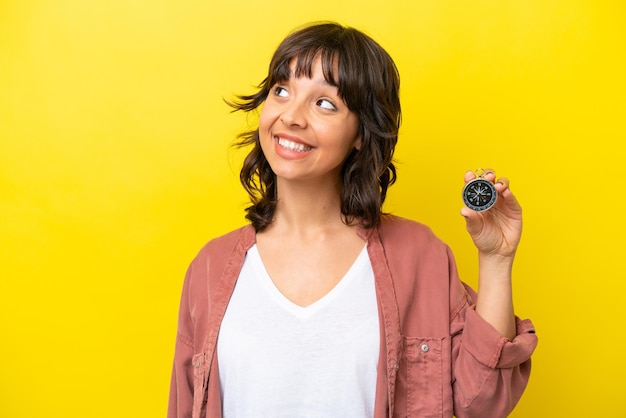 Young latin woman holding compass isolated on yellow background thinking an idea while looking up