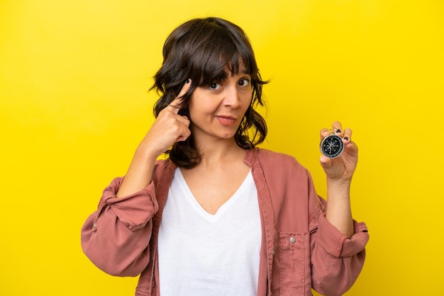 Young latin woman holding compass isolated on yellow background thinking an idea