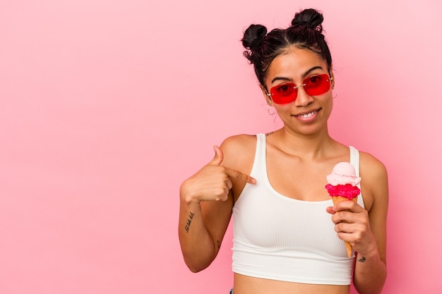 Young latin woman holding an ice cream isolated on pink background person pointing by hand to a shirt copy space, proud and confident