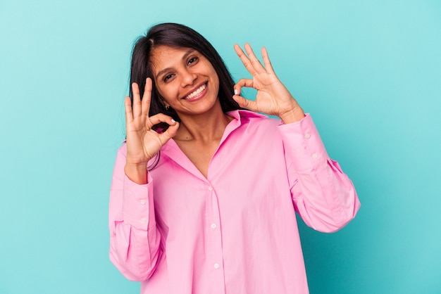 Young latin woman isolated on blue background cheerful and confident showing ok gesture.