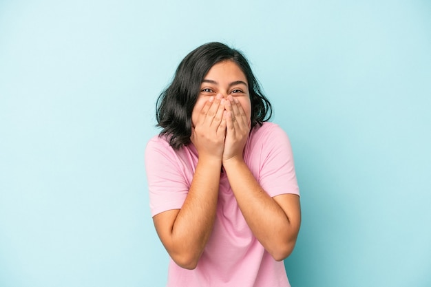 Young latin woman isolated on blue background laughing about something, covering mouth with hands.