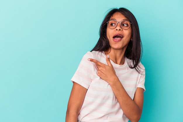 Young latin woman isolated on blue background points with thumb finger away, laughing and carefree.