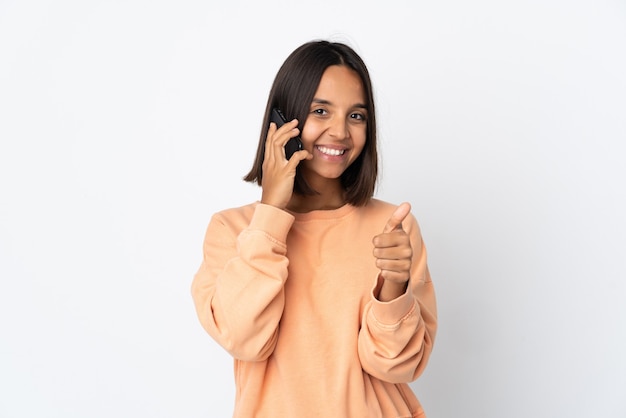 Young latin woman isolated on white background keeping a conversation with the mobile while doing thumbs up