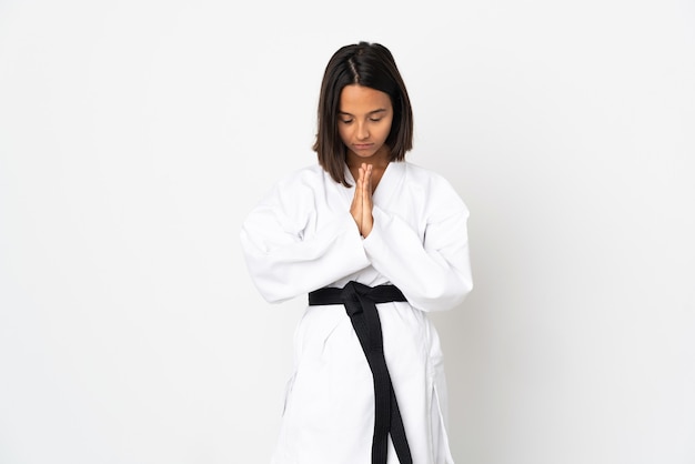 Young latin woman isolated on white wall doing karate and saluting