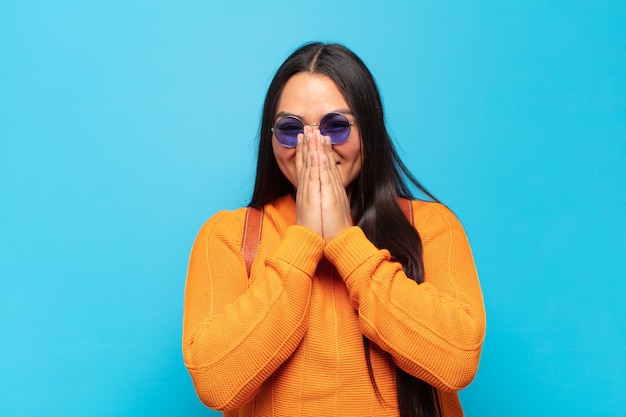 Young latin woman looking happy, cheerful, lucky and surprised covering mouth with both hands