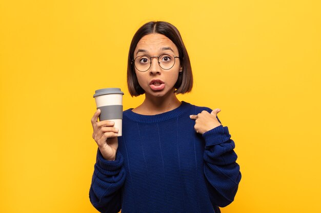 young latin woman looking shocked and surprised with mouth wide open, pointing to self