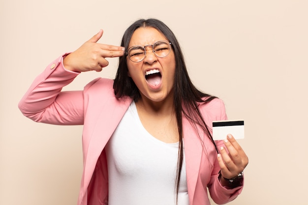 Young latin woman looking unhappy and stressed, suicide gesture making gun sign with hand, pointing to head