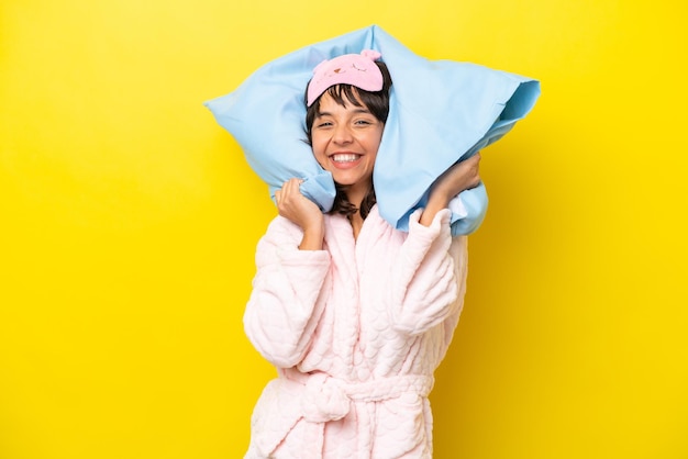 Young latin woman in pajamas isolated on yellow background