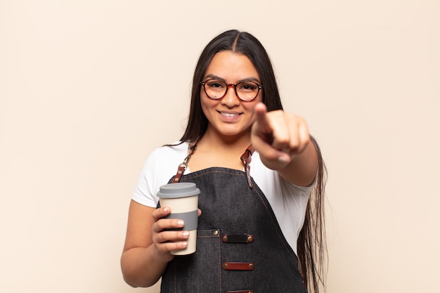 Young latin woman pointing at camera with a satisfied, confident, friendly smile