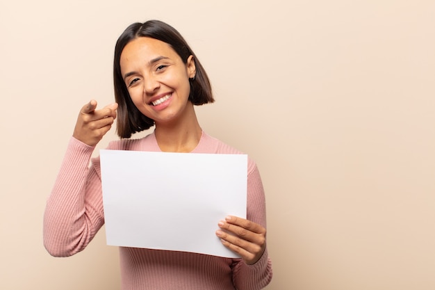 Young latin woman pointing at front with a satisfied, confident, friendly smile, choosing you