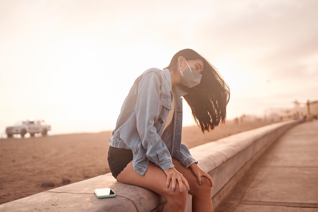 Young latin woman poses walking on the sand during a beautiful sunset Happy young woman with mask