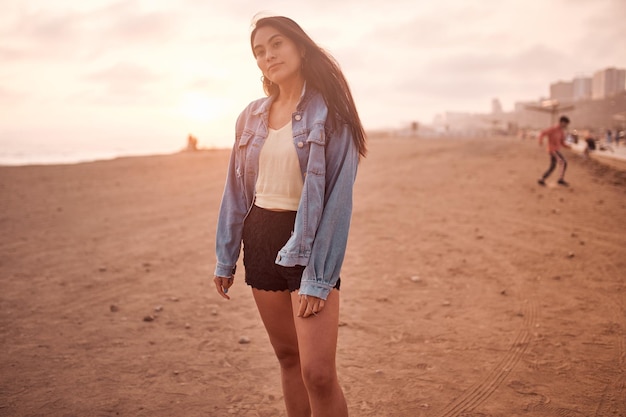 Young latin woman poses walking on the sand during a beautiful sunset