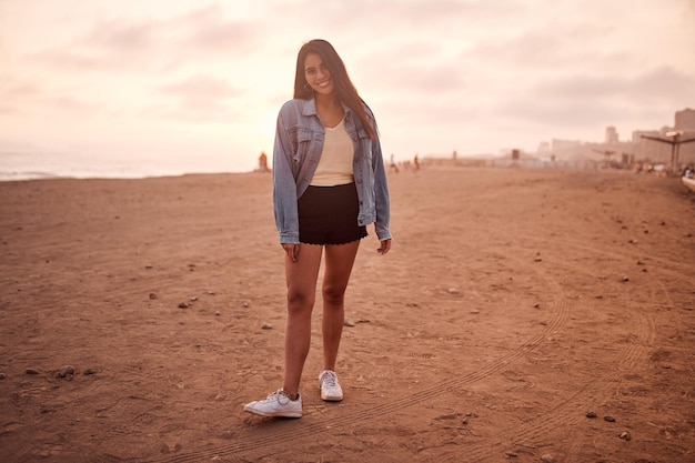 Young latin woman poses walking on the sand during a beautiful sunset