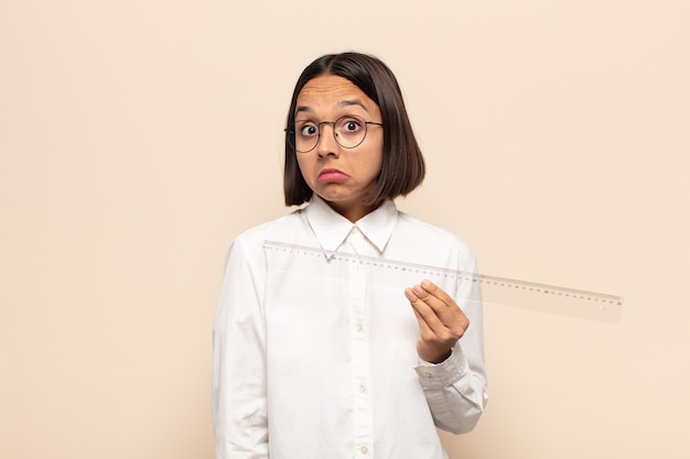 Young latin woman shrugging, feeling confused and uncertain, doubting with arms crossed and puzzled look