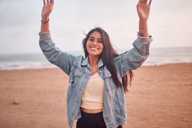 Young Latin woman smiles during a beautiful sunset Happy young woman with mask on the beach taking