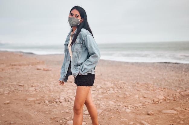 Young Latin woman smiles during a beautiful sunset Happy young woman with mask on the beach taking