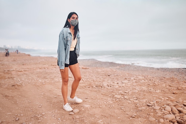 Young Latin woman smiles during a beautiful sunset Happy young woman with mask on the beach taking