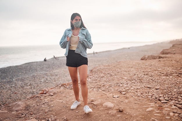 Young Latin woman smiles during a beautiful sunset Happy young woman with mask on the beach taking