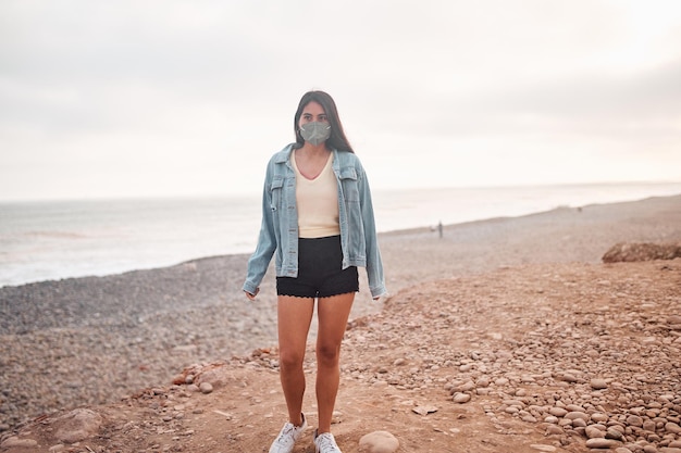 Young Latin woman smiles during a beautiful sunset Happy young woman with mask on the beach taking