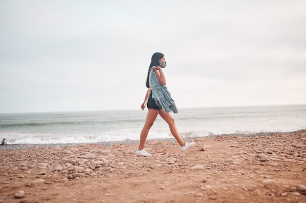 Young Latin woman smiles during a beautiful sunset Happy young woman with mask on the beach taking