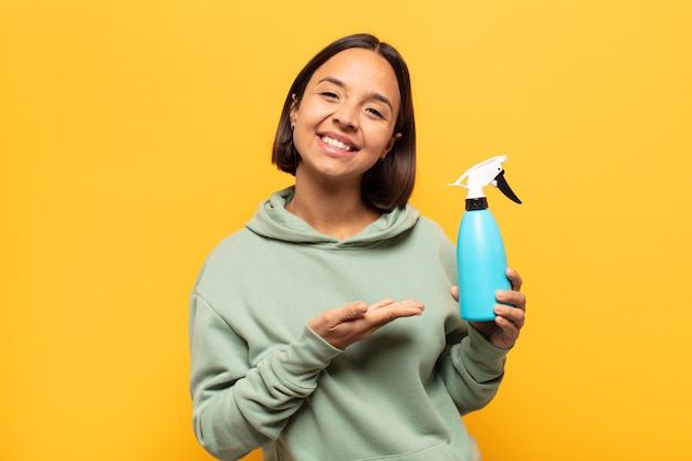 Young latin woman smiling cheerfully, feeling happy and showing a concept in copy space with palm of hand