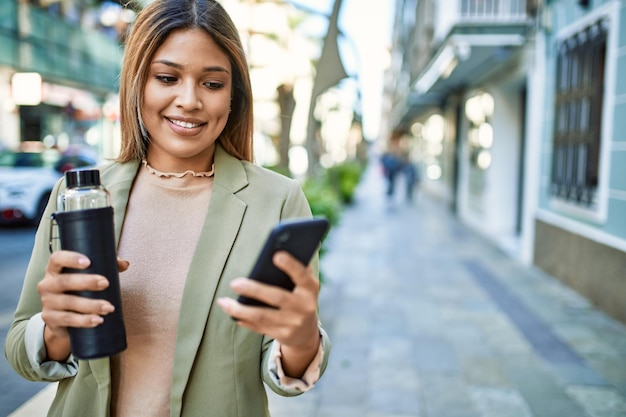 Young latin woman smiling confident using smartphone at street