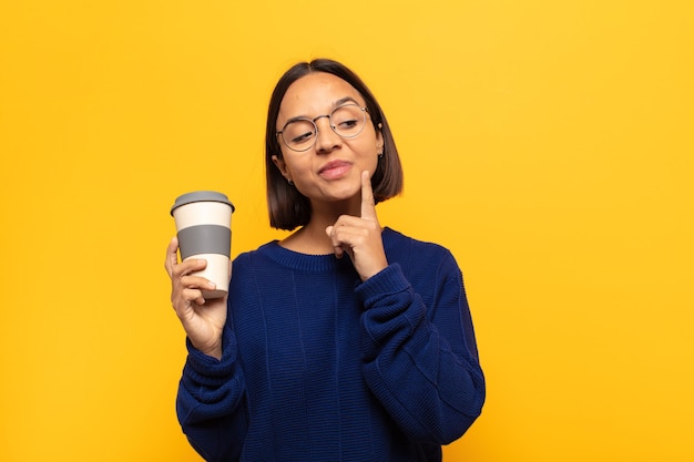 young latin woman smiling happily and daydreaming or doubting, looking to the side