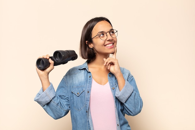 Young latin woman smiling happily and daydreaming or doubting, looking to the side