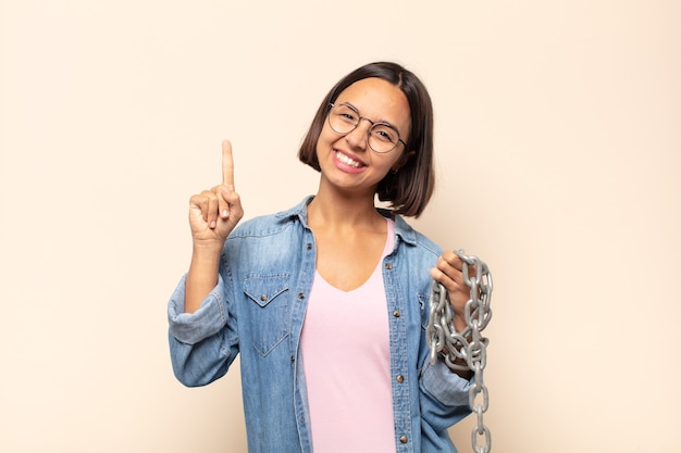 young latin woman smiling and looking friendly, showing number one or first with hand forward, counting down