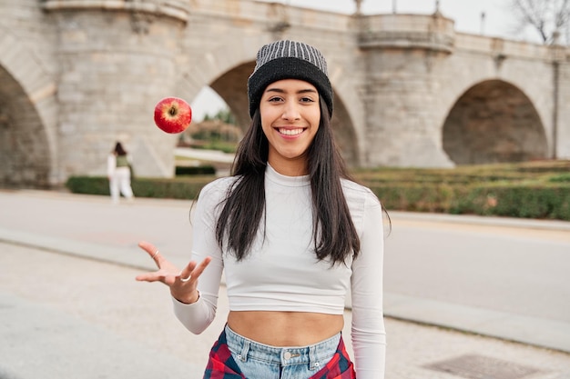 Young latin woman smiling and throwing an apple