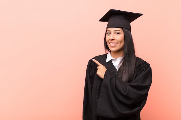 Young latin woman student smiling cheerfully, feeling happy and pointing to the side and upwards, showing object in copy space