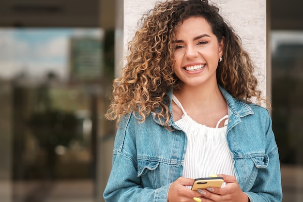 Young latin woman using her mobile phone while walking outdoors on the street. Urban concept.