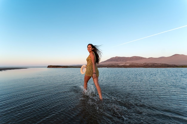 Young latin woman walking on through water happy and smiling outdoors, looking at the camera, back view