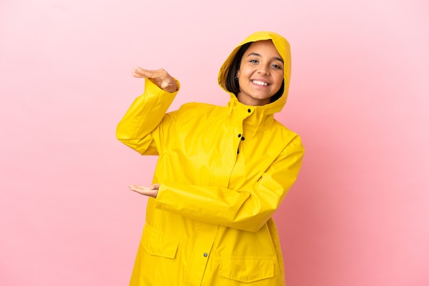 Young latin woman wearing a rainproof coat over isolated background holding copyspace to insert an ad