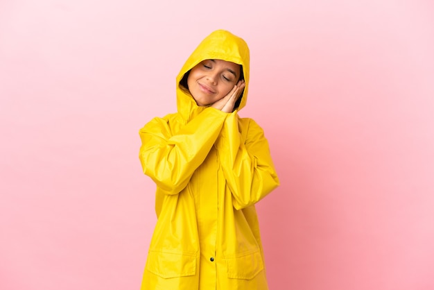 Young latin woman wearing a rainproof coat over isolated background making sleep gesture in dorable expression