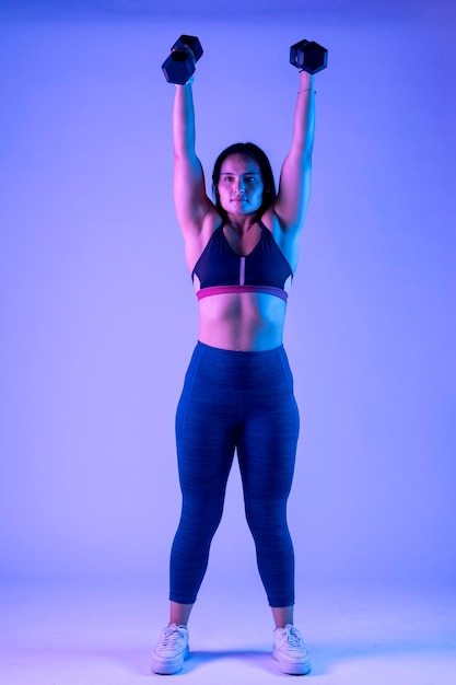 Young latin woman wearing sportswear doing shoulder press with two dumbbells