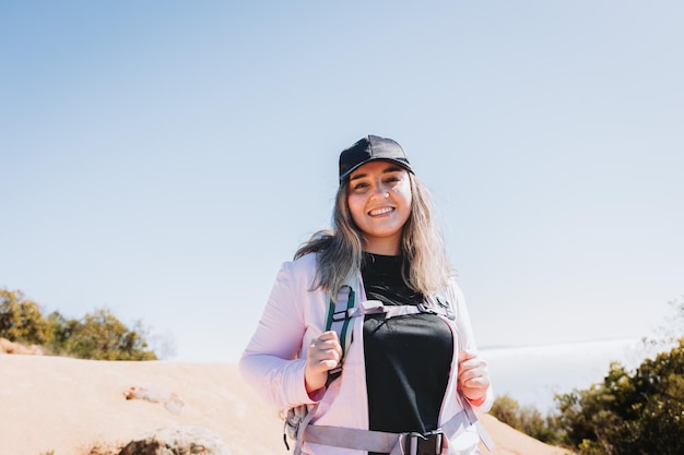 Young latin woman with backpack on, climbing a hill and hiking in a beautiful landscape.