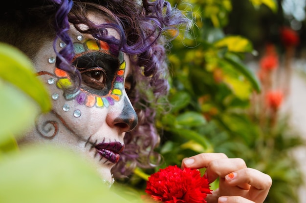 Young latin woman with catrina makeup standing among the bushes in the cemetery