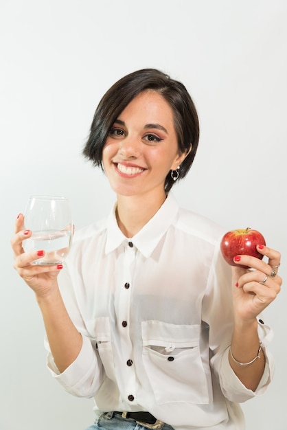 Young latin woman with glass of water in one hand and a red apple in the other hand