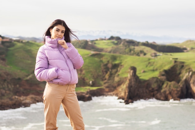 Young latin woman with purple coat covering her mouth and nose with it with a beautiful seascape