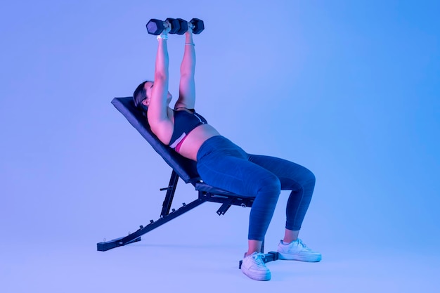 Young latin woman with sportswear doing chest press lying on a bench