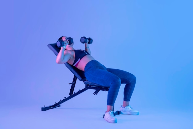 Young latin woman with sportswear doing chest press lying on a bench