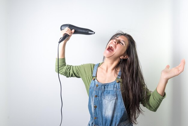 Young latina screaming open mouth drying hair combing hair hairdresser at home very long hair on neutral background