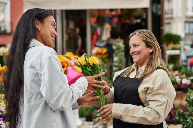 Young Latina woman purchasing vibrant flowers from a street vendor's stall handed by the gardener