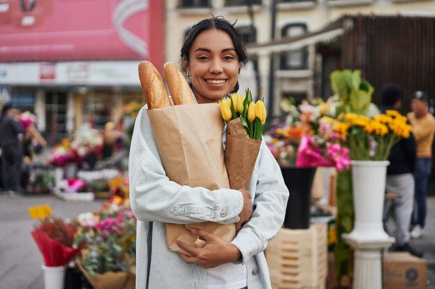 Young Latina woman smiling while buying yellow tulips and bread from a street vendor's stall