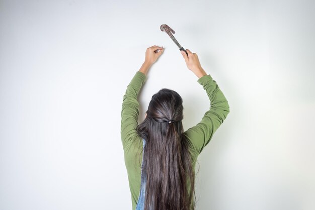 Young latina woman with back nailing a nail into the wall to hang a picture home work